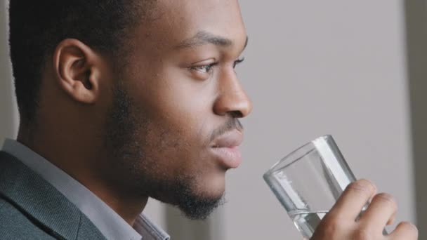 Primer plano feliz 30s hombre de etnia africana hombre de negocios en traje reflexiona reflexivamente beber vidrio agua purificada pura fresca. Comenzar el día Buenos hábitos de vida para una piel y un cuerpo sanos - Metraje, vídeo