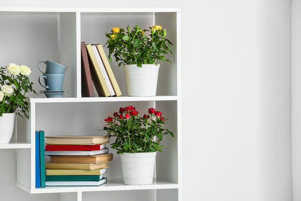 Hermosas rosas en macetas y libros en el estante cerca de la pared blanca - Foto, Imagen
