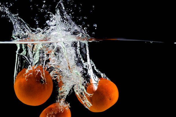 three tangerines fall into the water on a black background, copy space - 写真・画像