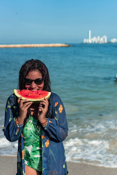 アフリカ系アメリカ人女性がビーチでスイカを食べる - 写真・画像