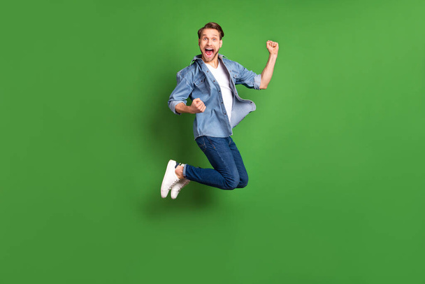 Full length body size photo of young guy jumping high gesturing like winner isolated bright green color background - Foto, immagini