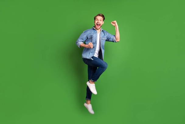Full length body size photo of young guy jumping happy gesturing like winner cheerful isolated vivid green color background - 写真・画像