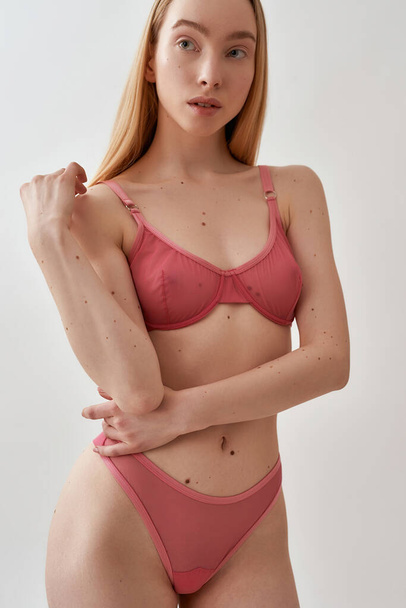 Sensual young caucasian woman with slim body wearing pink transparent underwear looking aside while posing isolated over light gray background - Φωτογραφία, εικόνα