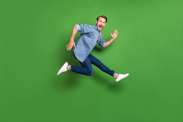 Full length body size side profile photo of young guy jumping up careless laughing isolated vibrant green color background - Zdjęcie, obraz