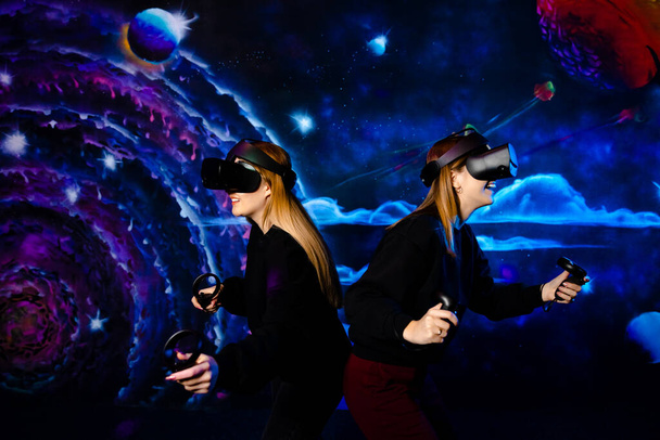 Deux jeunes filles sœurs amies avec des lunettes virtuelles s'amusent ensemble et jouent à des jeux vidéo - Photo, image