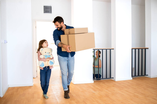 Happy father and daughter carrying boxes and toys while moving into new house. - Φωτογραφία, εικόνα