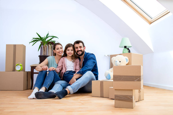 портрет счастливой улыбающейся кавказской семьи, находящейся в новом доме, и картонные коробки вокруг них. - Фото, изображение
