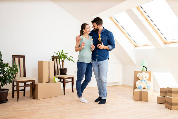 Young caucasian couple opening champagne bottle to celebrate moving into new house. - Photo, image
