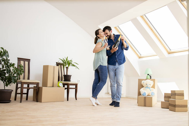 Young caucasian couple dancing and opening champagne bottle to celebrate moving into new house. - Foto, afbeelding