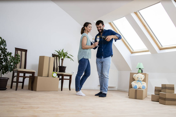 Young caucasian couple dancing and opening champagne bottle to celebrate moving into new home. - Photo, image