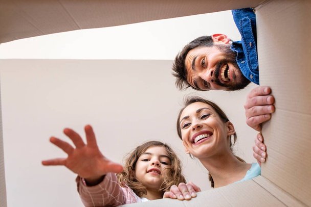 Low angle view of happy family opening cardboard box together and unpacking belongings. - Foto, immagini