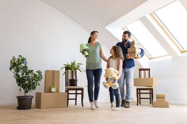 Happy caucasian family moving in new apartment with cute little girl carrying boxes and belongings. - 写真・画像