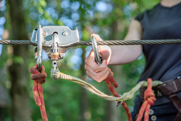 Forest Adventure Park. The woman fastens her carabiner and uses the climbing equipment. Overcome obstacles in the forest adventure park. Banner for advertising and place to insert text. - 写真・画像