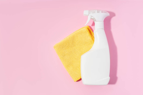 Weiße Reinigungs-Sprühflasche und gelber Lappen auf hellrosa Hintergrund. - Foto, Bild