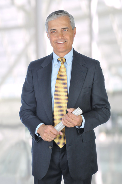 Middle aged businessman in a suit and tie standing in a modern office building holding a rolled up newspaper. Vertical Format - Photo, image