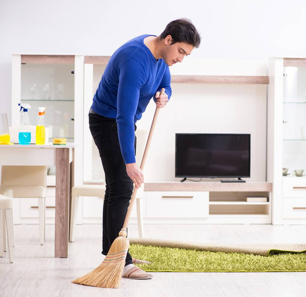 Young man cleaning floor with broom - Foto, Imagen