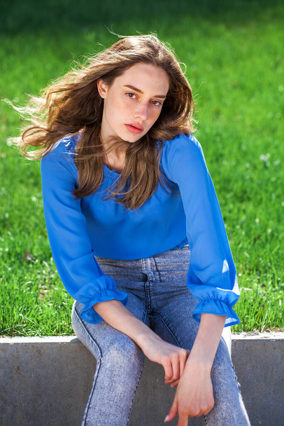 Young beautiful brunette girl in a blue blouse and gray jeans, summer park outdoor  - Fotoğraf, Görsel