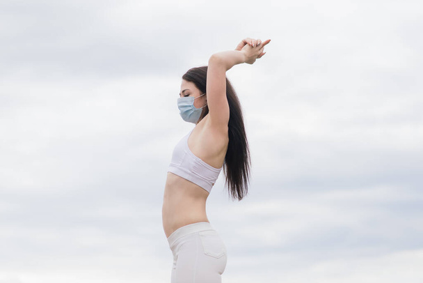 Sport during quarantine, coronavirus, covid. Young athletic woman wearing medical protective mask - Фото, изображение