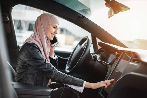 Arabada cep telefonuyla konuşan bir kadın gösterge paneline dokunuyor - Fotoğraf, Görsel