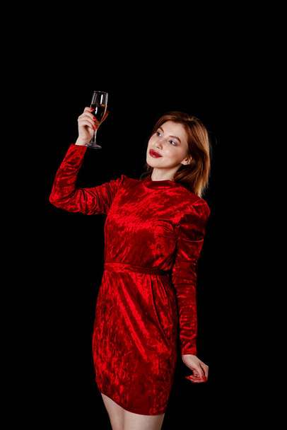 A brown-haired girl in a red dress raises a glass of champagne with her hand - Foto, imagen