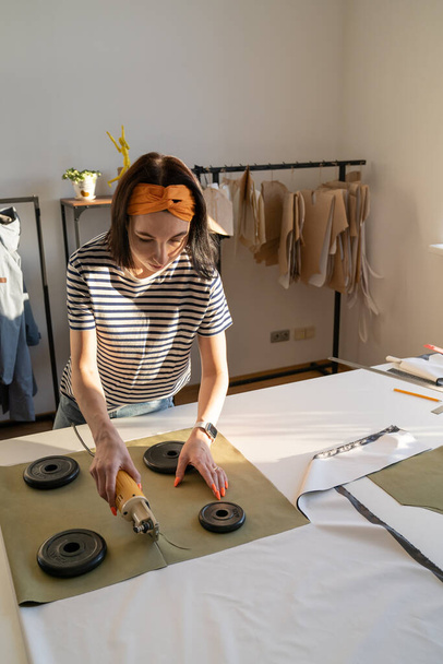 Machine de tissu de coupe d'utilisation de tailleur femelle, concepteur de vêtements de fille ou couturière travaillent sur une nouvelle collection - Photo, image