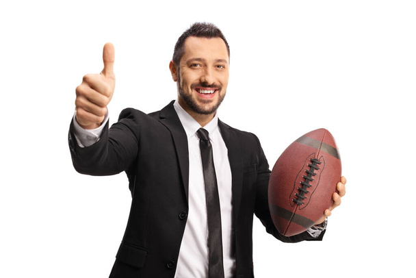 Smiling businessman holding a rugby ball and gesturing thumbs up isolated on white background - Foto, Imagem