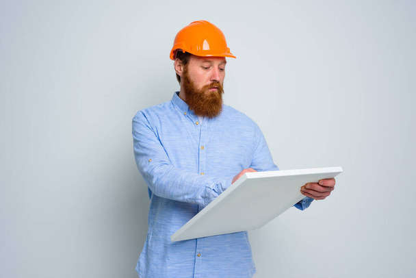 Vertrauensvoller Architekt mit Bart und orangefarbenem Helm skizziert - Foto, Bild
