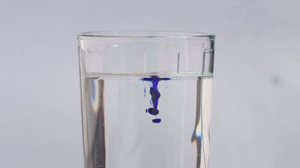 Beyaz zemin üzerinde duran saf su bardağına damlayan küçük açık mavi mürekkep damlaları. Yavaş yavaş sıvı karışımı görkemli bir sıvı.. - Video, Çekim