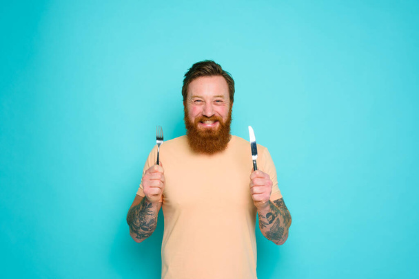 Boldog ember tetoválásokkal kész enni evőeszközökkel a kezében. - Fotó, kép