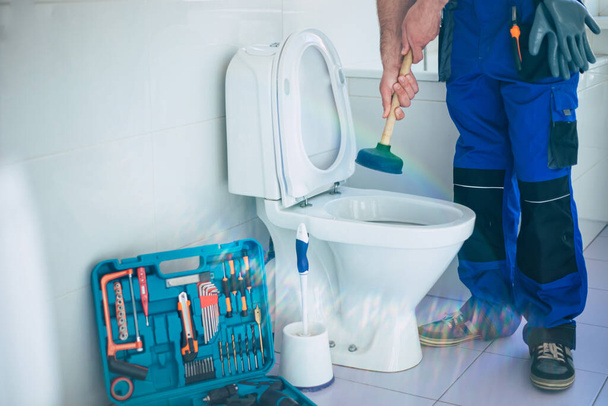 Professional plumber in uniform is repairing toilet bowl in the domestic bathroom with the help of tools - Фото, зображення