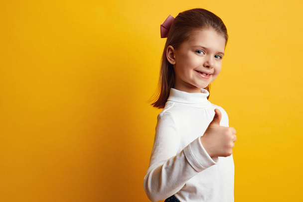 Optimiste fille enfant montrant pouces vers le haut sur fond jaune vif - Photo, image