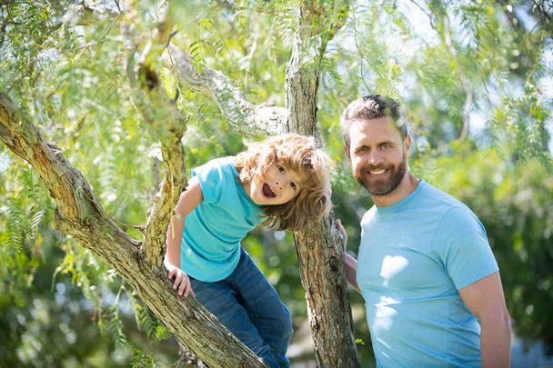 Щаслива сім'я. Батько і син посміхаються, сидячи на дереві. Сімейна забава. Дитинство та батьківство
 - Фото, зображення