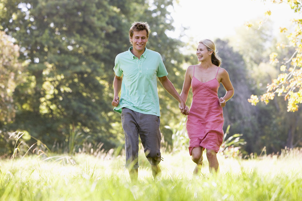 Couple running outdoors holding hands and smiling - Fotoğraf, Görsel