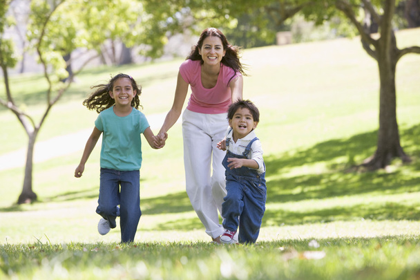 Mujer con dos niños pequeños corriendo al aire libre sonriendo
 - Foto, Imagen
