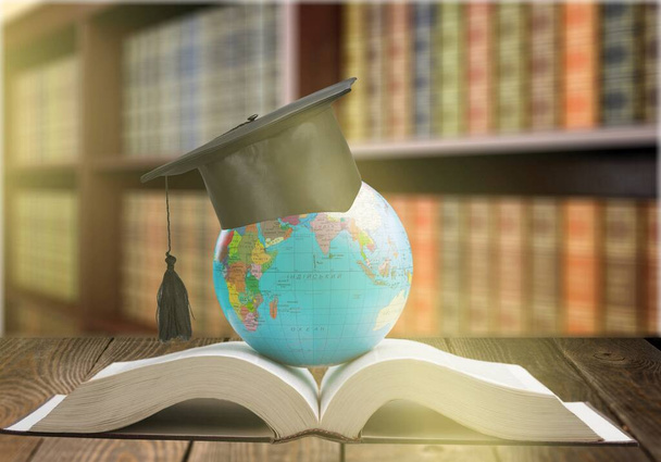 Education to learn study in world. Graduated student studying abroad international idea. Master degree hat on top globe book. Concept of graduate educational for long distane learning anywhere anytime - Фото, изображение