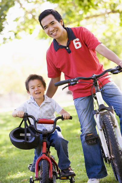 Man and young boy on bikes outdoors smiling - 写真・画像