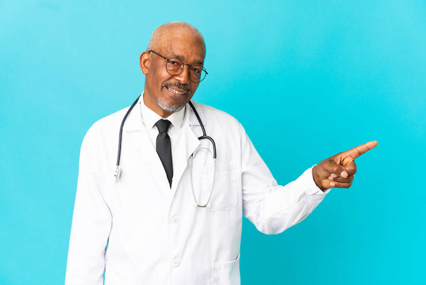 Senior arts man geïsoleerd op blauwe achtergrond wijzend vinger naar de zijkant - Foto, afbeelding