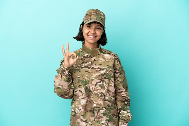 Wojskowe mieszane rasy kobieta odizolowana na niebieskim tle pokazuje znak ok palcami - Zdjęcie, obraz