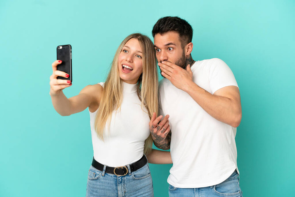 Młoda para na odizolowanym niebieskim tle robi selfie z telefonem - Zdjęcie, obraz