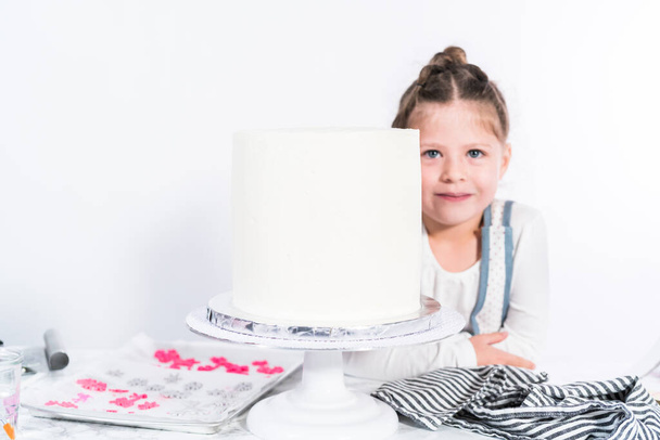 Petite fille aidant à cuire un grand gâteau funfetti avec glaçage blanc crème au beurre
. - Photo, image