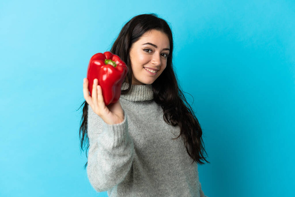 Young caucasian woman holding a pepper isolated on blue background with happy expression - Valokuva, kuva