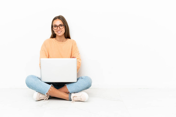 Young woman with a laptop sitting on the floor keeping the arms crossed in frontal position - Foto, Imagen