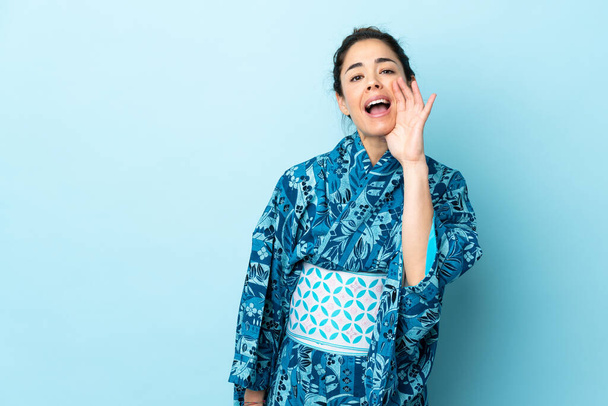 Woman wearing kimono over isolated background shouting with mouth wide open - Fotó, kép
