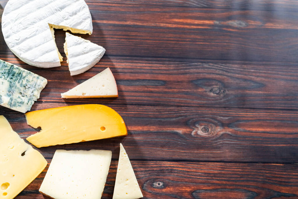 Acostado. Variedad de grandes cuñas de queso gourmet sobre un fondo de madera oscura. - Foto, imagen