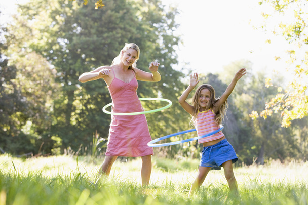 Woman and young girl outdoors using hula hoops and smiling - Fotoğraf, Görsel