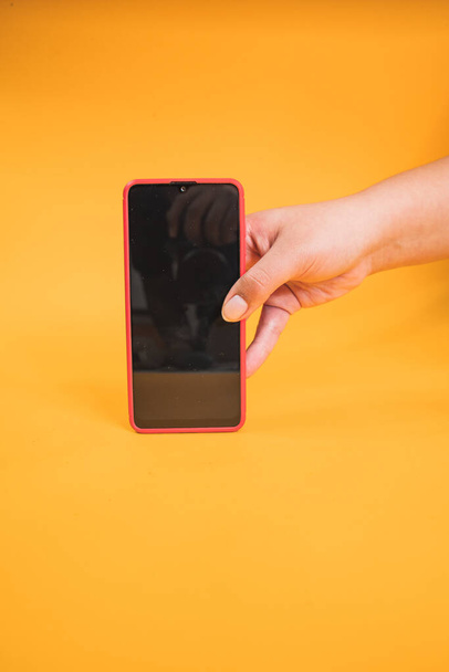 A vertical shot of a female holding a mobile phone isolated on a yellow background - Photo, image