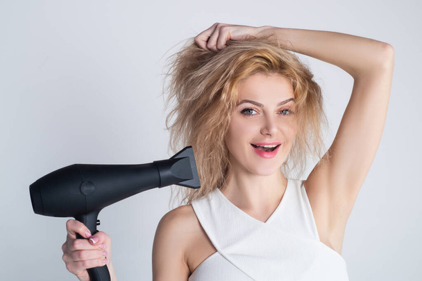 Health hair and beauty concept. Girl with blonde hair using hairdryer. Young attractive happy laughing blonde woman with hair dryer. Hairstyle, hairdressing concept. - 写真・画像