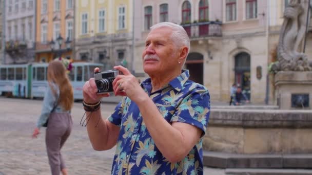 Vanhempi mies turisti ottaa kuvia valokuva kamera kesällä kaupungin keskustassa, elämä eläkkeelle - Materiaali, video
