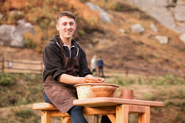 Pottenbakker werkt met klei. Jongeman pottenbakker op zijn werkplaats met natuur achtergrond - Foto, afbeelding