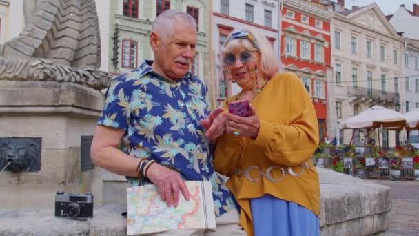 Старшая стильная пара туристов мужчина, женщина, бабушка, дедушка ищет способ с помощью смартфона - Кадры, видео